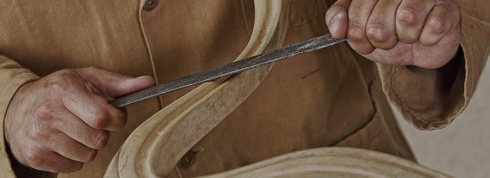Le mani di un artigiano che rifiniscono con la lima una sagoma in legno